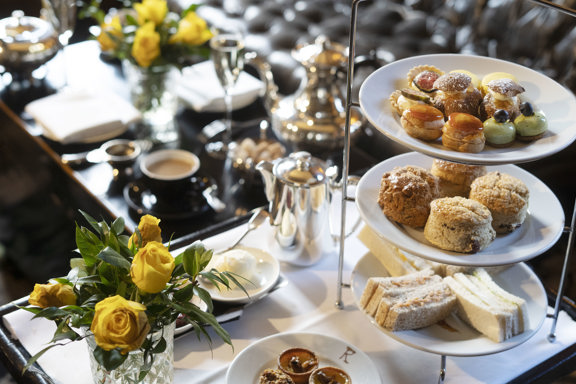 Afternoon tea in the Yellow Room at Prestonfield, featuring three-tier stand of sandwiches, scones and pastries alongside a range of teas, champagne and fresh yellow roses, a luxurious experience ideal for afternoon tea vouchers in Edinburgh.
